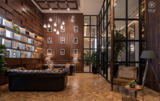 Không gian tiếp khách tại Feliz En Vista Quận 2 sử dụng nội thất gỗ trầm, ghế sofa da và hệ đèn thả trần, kết hợp các ô kính lớn tạo nên phong cách ấm cúng và sang trọng.