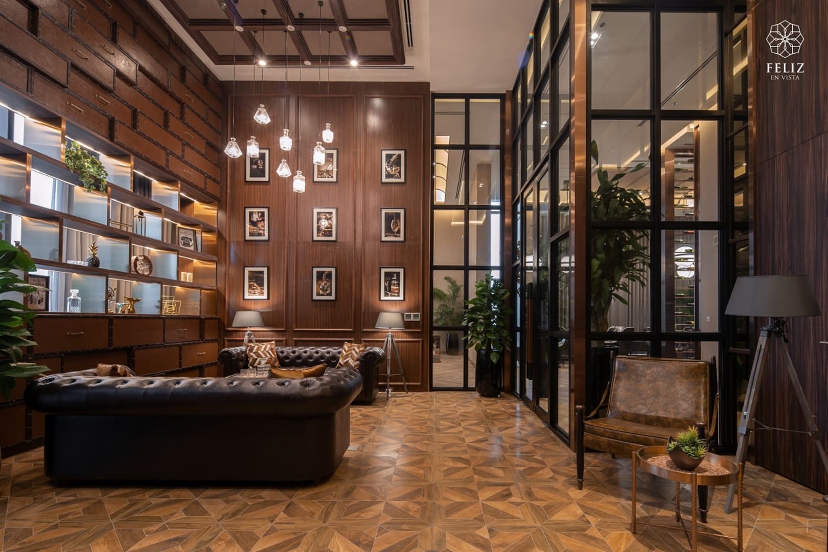 Không gian tiếp khách tại Feliz En Vista Quận 2 sử dụng nội thất gỗ trầm, ghế sofa da và hệ đèn thả trần, kết hợp các ô kính lớn tạo nên phong cách ấm cúng và sang trọng.