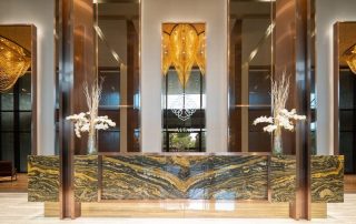 Sảnh lễ tân tại Feliz En Vista Quận 2 gây ấn tượng với quầy ốp đá vân nổi bật, đèn trang trí sắc vàng và thiết kế trần cao, mang đến không gian đón tiếp trang nhã ngay từ lối vào.